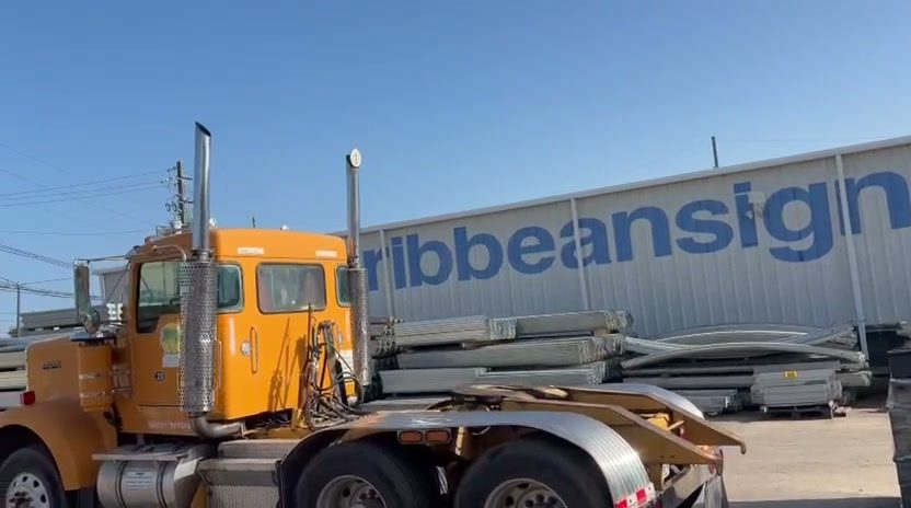 Camión de Caribbean Sign Supply frente al almacén con inventario de guardarraíl